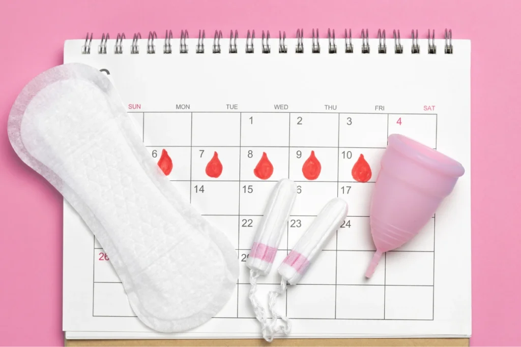 Calendar showing menstrual bleeding with a sanitary pad, tampons, and menstrual cup, representing abnormal uterine bleeding and irregular menstrual cycle symptoms.